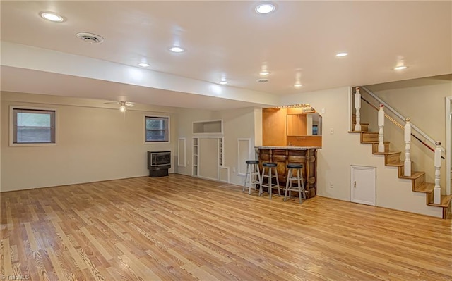 unfurnished living room with light wood-style flooring, recessed lighting, stairway, a dry bar, and a wood stove