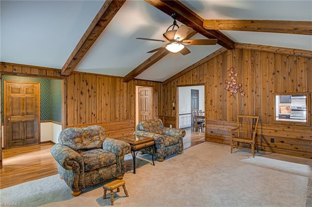 living area with lofted ceiling with beams, carpet floors, wood walls, and ceiling fan