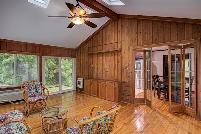 living area featuring wooden walls, heating unit, light wood finished floors, ceiling fan, and lofted ceiling with skylight