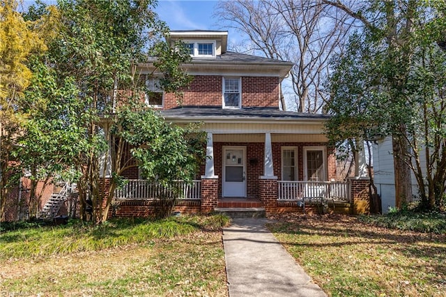 american foursquare style home featuring a porch, brick siding, and a front yard