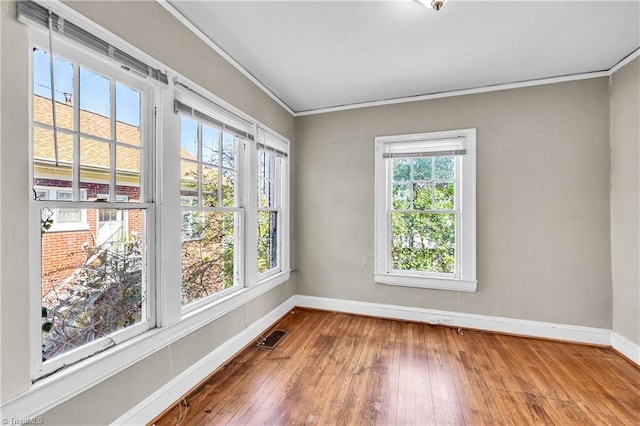 spare room with hardwood / wood-style floors, a wealth of natural light, baseboards, and ornamental molding