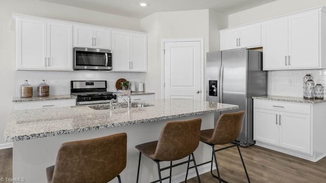 kitchen with light stone counters, appliances with stainless steel finishes, an island with sink, decorative backsplash, and white cabinets