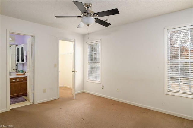 unfurnished bedroom with a spacious closet, a textured ceiling, ensuite bath, light colored carpet, and ceiling fan