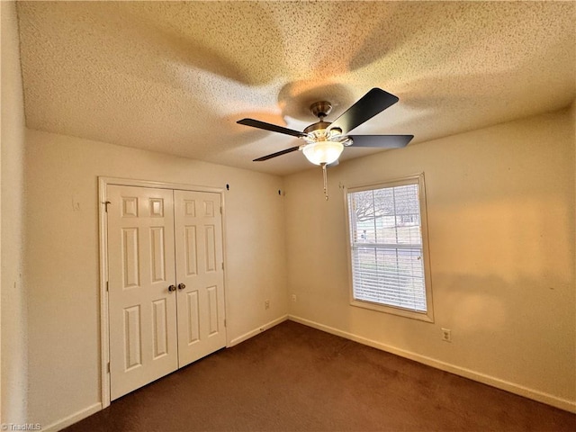 unfurnished bedroom featuring a closet, ceiling fan, dark carpet, and a textured ceiling