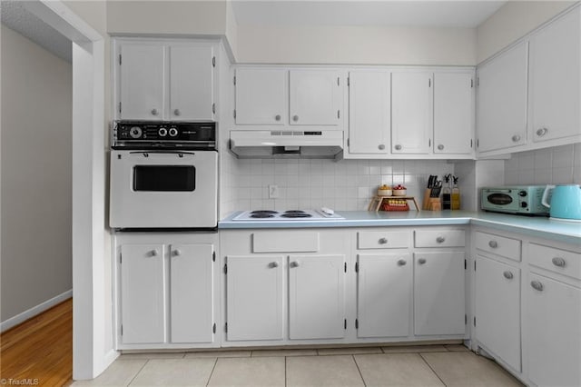 kitchen featuring white appliances, white cabinets, light countertops, under cabinet range hood, and backsplash