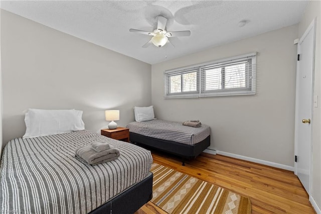 bedroom featuring ceiling fan, a textured ceiling, baseboards, and wood finished floors