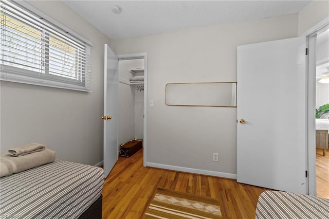 bedroom with baseboards, wood finished floors, a spacious closet, a textured ceiling, and a closet