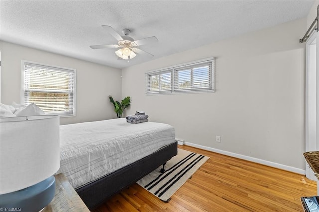 bedroom featuring light wood finished floors, multiple windows, baseboards, and a textured ceiling