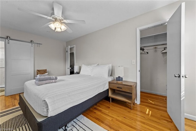 bedroom with a barn door, a ceiling fan, a closet, light wood-type flooring, and a walk in closet