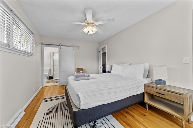 bedroom featuring a barn door, a ceiling fan, ensuite bath, light wood-type flooring, and baseboards