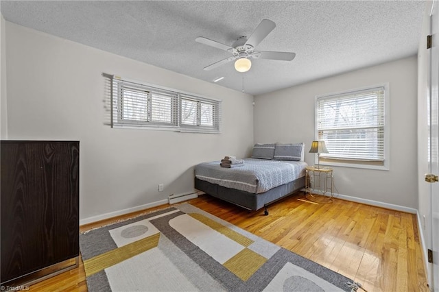 bedroom featuring hardwood / wood-style flooring, multiple windows, and a baseboard heating unit