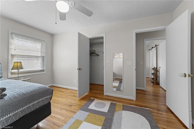 bedroom with a textured ceiling, a spacious closet, a barn door, and wood finished floors