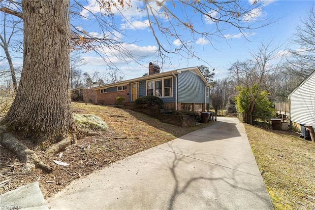 view of side of home featuring driveway, a chimney, and brick siding