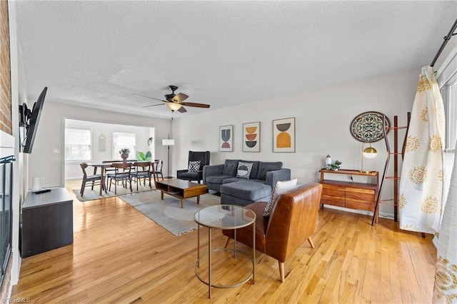 living room with light wood-type flooring, ceiling fan, and a textured ceiling