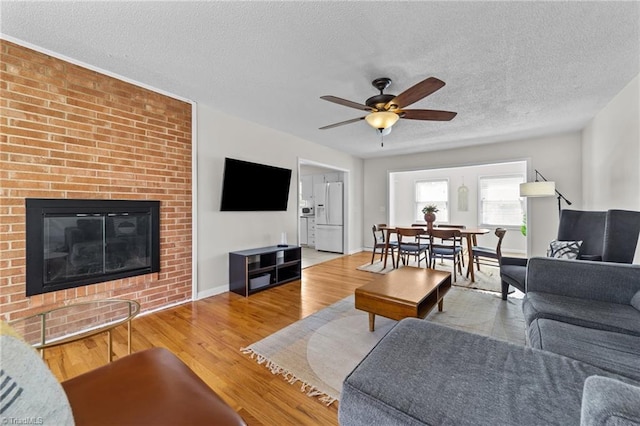 living room featuring a textured ceiling, a fireplace, wood finished floors, a ceiling fan, and baseboards