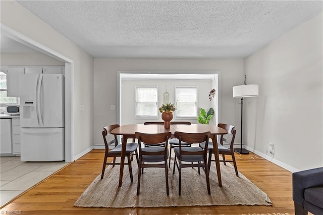 dining space featuring light wood-style floors, baseboards, and a textured ceiling