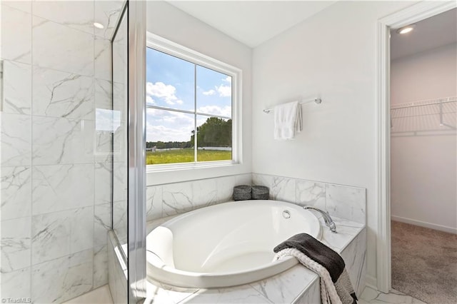 full bathroom featuring a walk in closet, a garden tub, and a marble finish shower