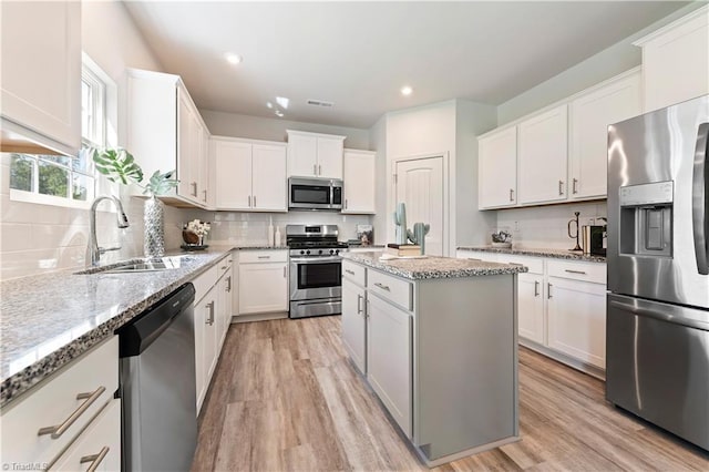 kitchen featuring light stone counters, appliances with stainless steel finishes, a sink, light wood-style flooring, and a center island