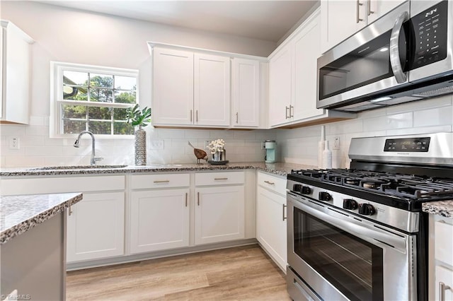 kitchen featuring white cabinets, light stone counters, a sink, appliances with stainless steel finishes, and backsplash