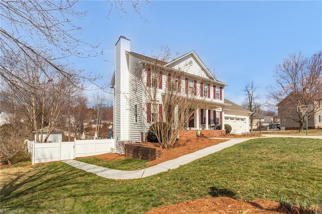 colonial home featuring a chimney, an attached garage, fence, driveway, and a front lawn