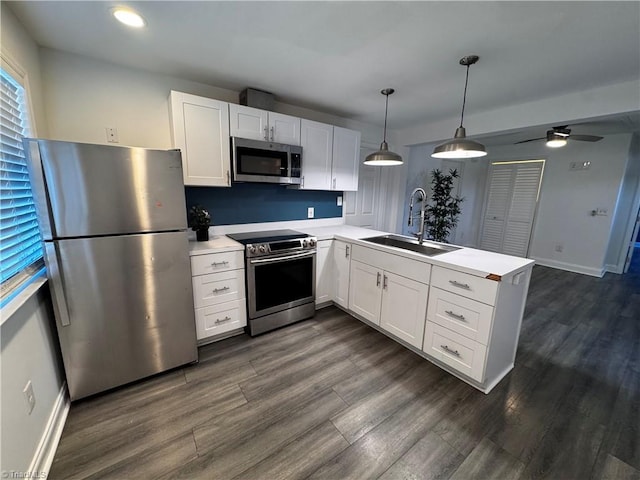 kitchen with kitchen peninsula, appliances with stainless steel finishes, sink, white cabinetry, and hanging light fixtures