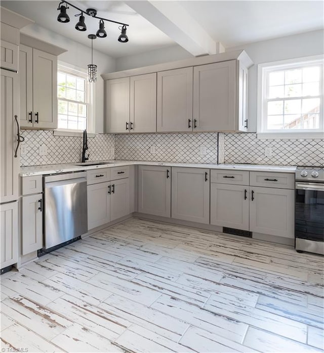 kitchen with appliances with stainless steel finishes, light wood-type flooring, backsplash, sink, and hanging light fixtures