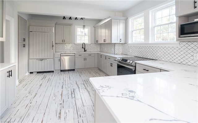 kitchen featuring light stone countertops, sink, backsplash, pendant lighting, and appliances with stainless steel finishes