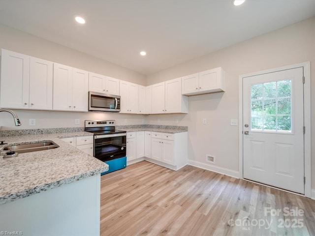 kitchen with white cabinets, sink, light hardwood / wood-style flooring, light stone countertops, and appliances with stainless steel finishes