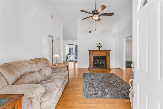 living room featuring ceiling fan, light wood-type flooring, a fireplace, and high vaulted ceiling