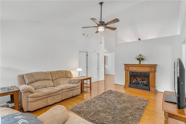 living room with ceiling fan, high vaulted ceiling, a fireplace, and light wood-style floors