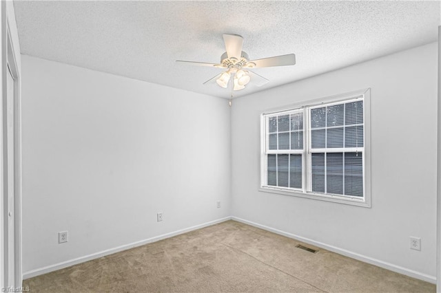 spare room with carpet floors, visible vents, a ceiling fan, a textured ceiling, and baseboards