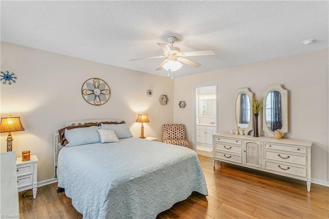 bedroom featuring a textured ceiling, baseboards, wood finished floors, and connected bathroom