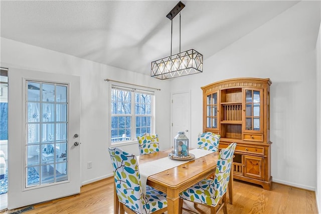 dining space with light wood-type flooring, visible vents, vaulted ceiling, and baseboards