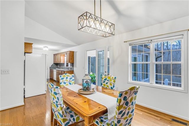 dining space featuring light wood-type flooring, vaulted ceiling, visible vents, and plenty of natural light