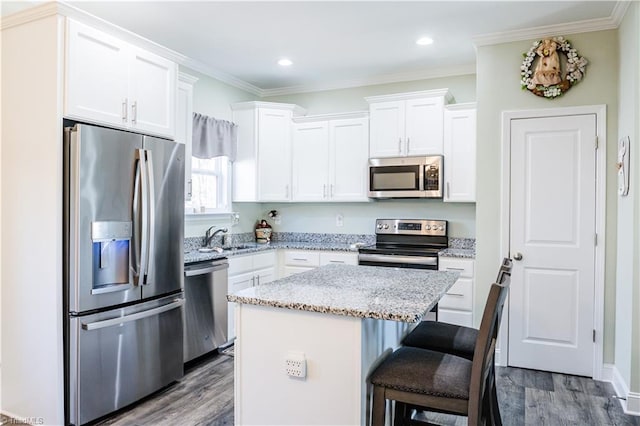 kitchen with a kitchen bar, a center island, appliances with stainless steel finishes, hardwood / wood-style flooring, and white cabinets