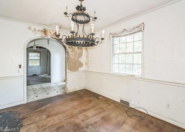 unfurnished dining area featuring dark wood-type flooring, crown molding, and a chandelier