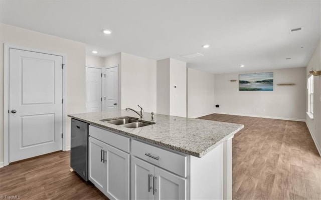 kitchen featuring dishwasher, an island with sink, a sink, and light wood-style flooring