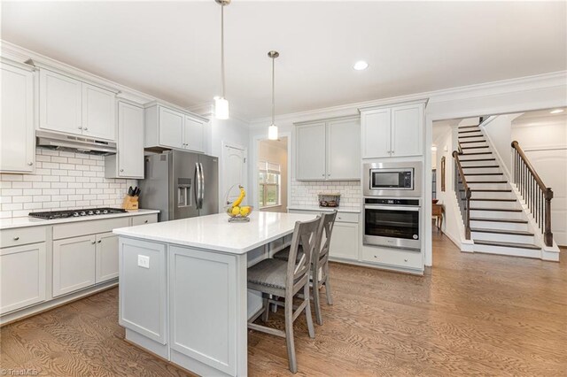 kitchen featuring light hardwood / wood-style floors, a kitchen island, white cabinetry, appliances with stainless steel finishes, and decorative light fixtures