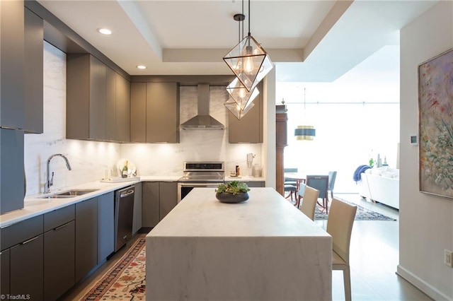 kitchen with pendant lighting, sink, appliances with stainless steel finishes, a kitchen island, and wall chimney exhaust hood