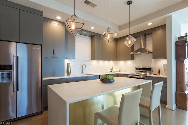 kitchen with wall chimney range hood, sink, a breakfast bar area, hanging light fixtures, and stainless steel appliances