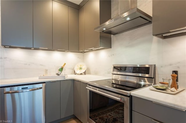 kitchen featuring gray cabinetry, wall chimney exhaust hood, and appliances with stainless steel finishes