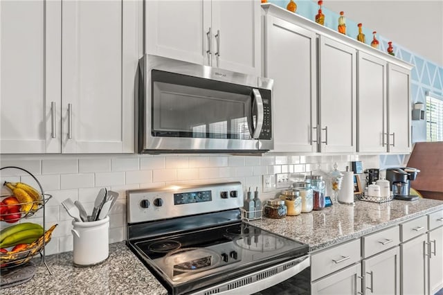 kitchen featuring appliances with stainless steel finishes, white cabinets, decorative backsplash, and light stone countertops