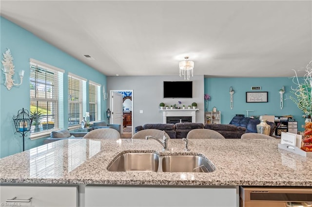 kitchen with dishwasher, light stone counters, open floor plan, and a sink