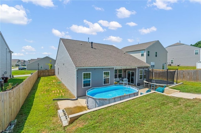 rear view of house with a fenced backyard, a lawn, a residential view, a fenced in pool, and a trampoline