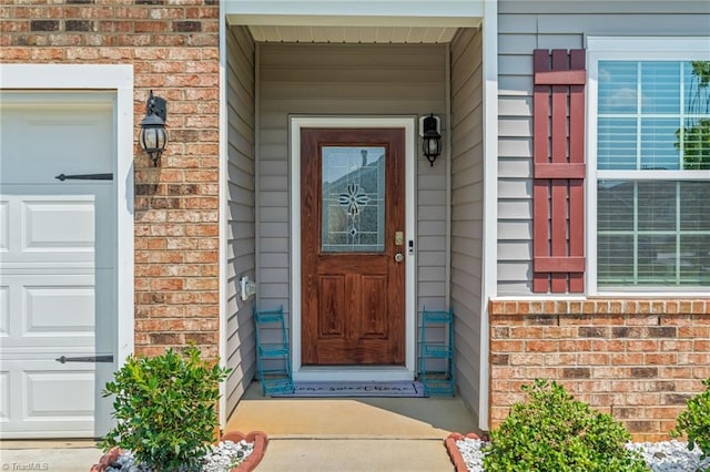 view of exterior entry featuring a garage and brick siding