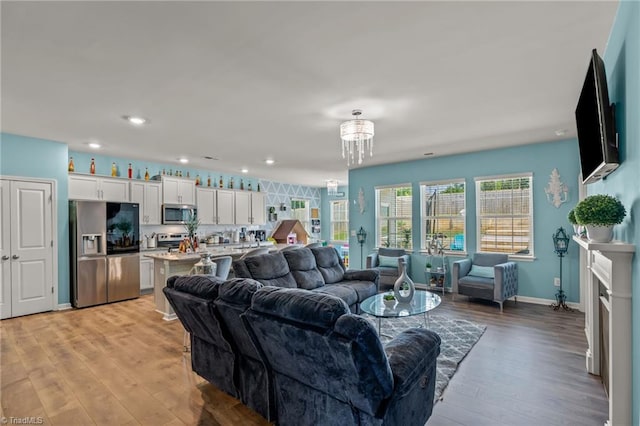 living room featuring baseboards, light wood-style flooring, an inviting chandelier, a fireplace, and recessed lighting