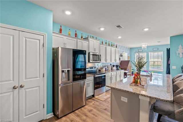 kitchen featuring a center island with sink, visible vents, white cabinets, appliances with stainless steel finishes, and a breakfast bar