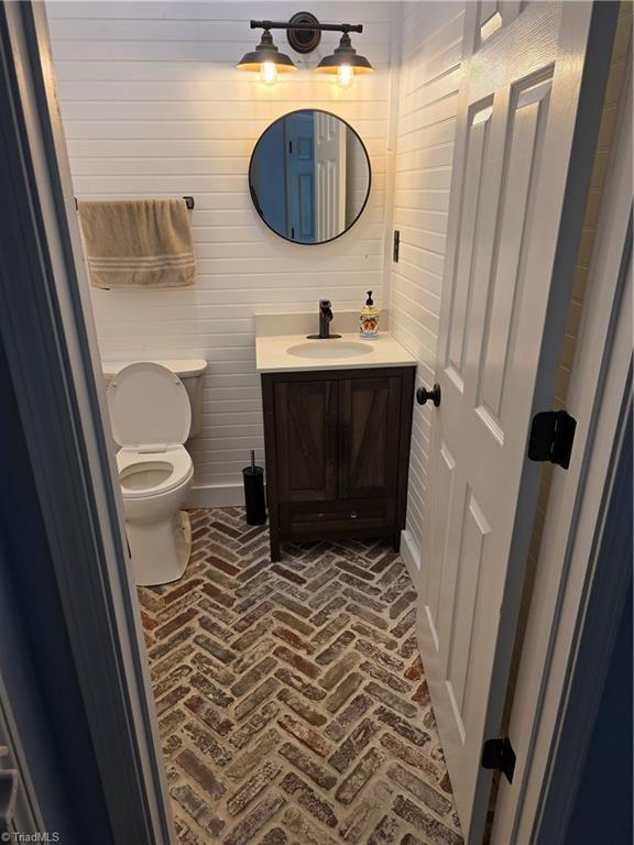 1030 Still Point Dr, Winston-Salem, NC 27103 - half bathroom with vanity, brick floors, toilet, and wooden walls