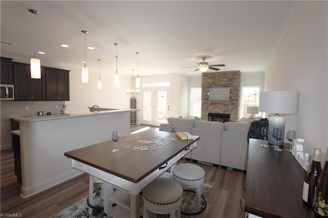 kitchen with a stone fireplace, dark hardwood / wood-style floors, ceiling fan, and pendant lighting