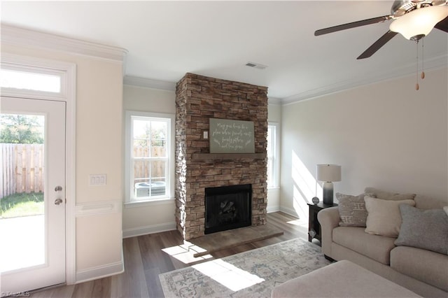 living room with a stone fireplace, dark hardwood / wood-style flooring, ornamental molding, and ceiling fan